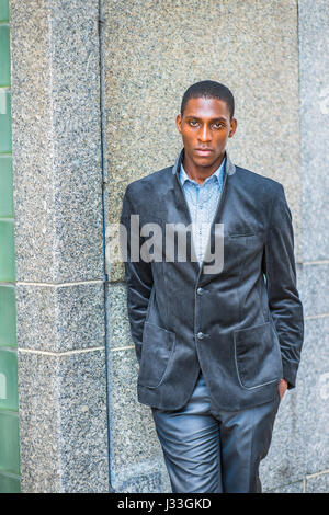 Young African American Mann mit neuen Stil schwarz Blazer, zwei Hände in den Taschen, stehend gegen die Wall Street in New York, indem ernst lookin Stockfoto