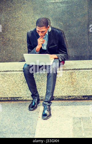 Young African American Mann mit schwarzen Blazer, Hosen, Leder-Schuhe, sitzen auf Marmor Bank in New York, auf der Suche nach unten, hand berühren Kinn, arbeiten Stockfoto