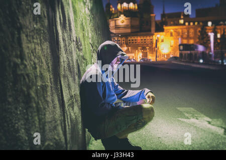 Traurig und einsam Mann mit Kapuze sitzen gegen eine Wand in der Nacht Stockfoto