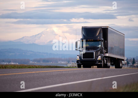 Stilvolle schwarze moderne leistungsstarke Sattelschlepper und Anhänger mit einem schwarzen Dach Spoiler Cockpit macht Fracht auf Versand entlang der malerischen Straße mit Blick Stockfoto