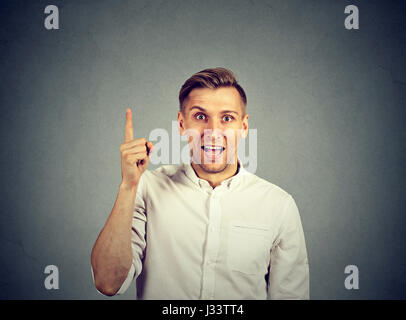 Porträt junger Mann hat eine Idee, mit Finger zeigen bis auf graue Wand Hintergrund isoliert. Aufgeregt Geschäftsmann mit Lösung des Problems. Gesicht Ausdruck, b Stockfoto