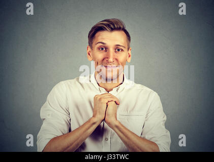 Freundlicher junger Mann zeigt gefalteten Händen, bitte schön isoliert auf grauem Hintergrund. Menschliche Emotionen Gesichtsausdruck Gefühle, Körpersprache Stockfoto