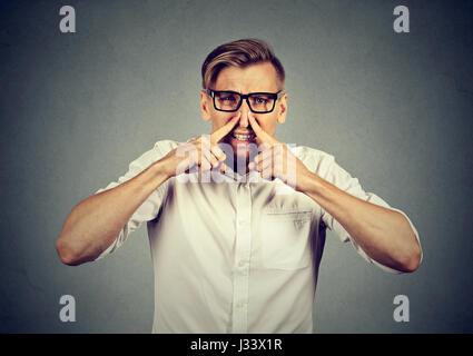 angewidert Mann Prisen Nase mit den Fingern sieht mit Ekel etwas schlechten Geruch auf grauem Hintergrund isoliert stinkt. Menschliches Gesicht Ausdruck Körpersprache Stockfoto