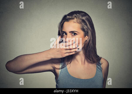 Closeup Portrait von Angst, junge Frau, die den Mund mit der Hand ihr auf graue Wand Hintergrund isoliert Stockfoto