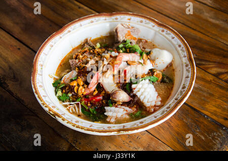 Spezielle scharfe Nudelsuppe oder Nudeln Tom Yam Suppe thai-Stil mit Meeresfrüchten und weich gekochtes Ei und knusprige Wan-Tan, Schweinefleisch und andere Gewürze auf Holz Stockfoto