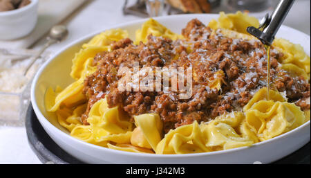 Gießen Olivenöl über köstlich dampfenden Tortellini in Bolognese-sauce Stockfoto