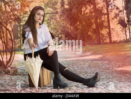 In voller Länge Portrait von junge Frau sitzt auf Vintage Koffer mit einem Regenschirm. Stockfoto