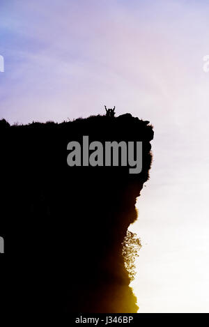 Schwarze Silhouette am Himmelshintergrund von zwei touristischen stehend Arme ausgestreckt zufrieden mit Erfolg am Spitzberg in der Nähe der Klippe bei Sonnenaufgang an Phu Stockfoto