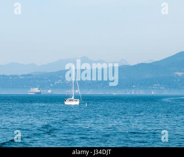 An einem trüben Tag warten private Boote und Handelsschiffe in der English Bay außerhalb von Vancouver, BC. Vom Vanier Park aus gesehen. Stockfoto