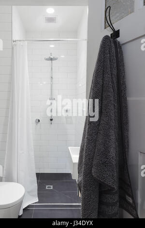 Kleine weiße geflieste Badezimmer mit Dusche und WC und hängenden Handtuch an einem Haken Stockfoto