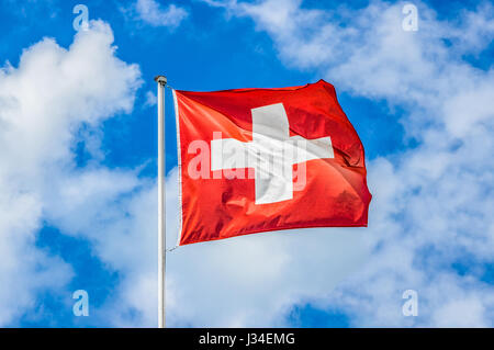 Klassische Ansicht der Nationalflagge der Schweiz winken in den Wind gegen blauen Himmel und Wolken an einem sonnigen Tag im Sommer Stockfoto