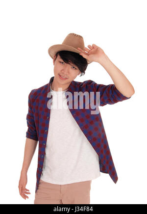 Glücklicher koreanische Teenager in einem karierten Hemd hält einen Hut auf dem Kopf stehend für weißen Hintergrund isoliert. Stockfoto