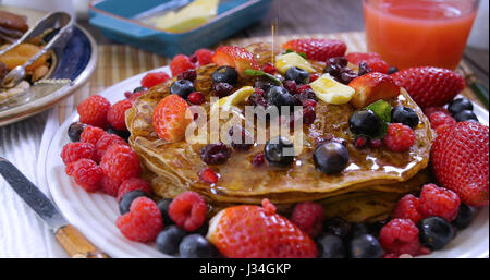 Ahornsirup in Strömen über ein Frühstück mit Pfannkuchen mit Beeren und getrockneten Früchten Stockfoto
