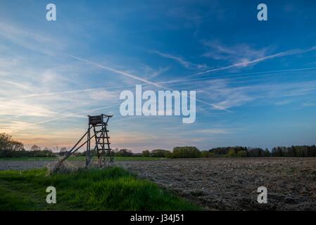 Horizontale Foto von hölzernen Jagd Turm Schutz neben braune Feder Feld mit einem Rasen auf Seite erfasst nach Sonnenuntergang mit blauen Himmel im Hintergrund Witz Stockfoto