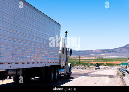 Weiße klassische Semi Truck und Trailer mit Reflexion auf der Straße mit Berg im Hintergrund Stockfoto