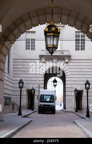 Ein kleiner Lkw mit einem Feld für die lokale Zustellung von Waren, die in der Stadt auf einer Straße in der Nähe des Gebäudes mit gewölbten Passagen und Laternen. Stockfoto