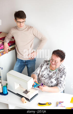 Patchwork und Quilting - eine ältere Frau Schneider bereitet schneiden farbigen Stoffstücke für Nähmaschinen, der junge Mann Uhren ihre Arbeit Stockfoto