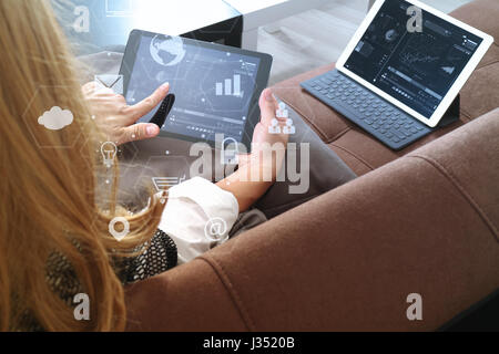 Brünette Frau mit digitalen Talet und Laptop-Computer auf Sofa im Wohnzimmer mit virtuellen Schnittstelle grafische Symbole Netzwerkdiagramm Stockfoto