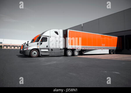 Zwei modernen professionellen kommerziellen Semi Trucks in Grau und Orange mit trockenen van Anhänger stehen in das Dock auf dem Gebiet der Transport Lager Stockfoto