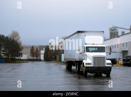 Weiß Semi Truck mit trockenen van Trailer mit Tag cab für lokale Datenverkehr, der Regen auf der nassen Straße zum Ort der industriellen Zone Lagergebäude Stockfoto