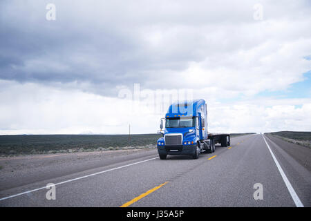 Moderne leistungsfähige Big Rig blue Semi Truck mit einer Kabine und einem flachen Bett Aluminium Anhänger ohne Last bewegt sich mit hoher Geschwindigkeit auf einer Geraden als Pfeil Stockfoto