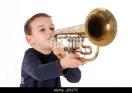 kleiner Junge bläst in eine Trompete vor weißem Hintergrund Stockfoto