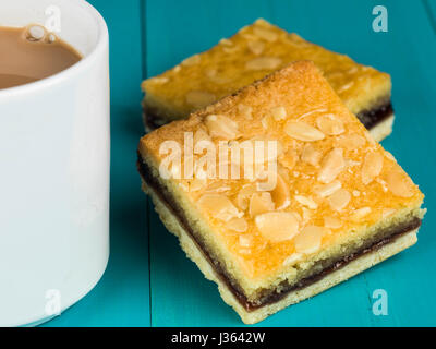 Cherry Bakewell Kuchen mit einer Tasse oder Becher Tee oder Kaffee vor einem blauen Hintergrund Stockfoto