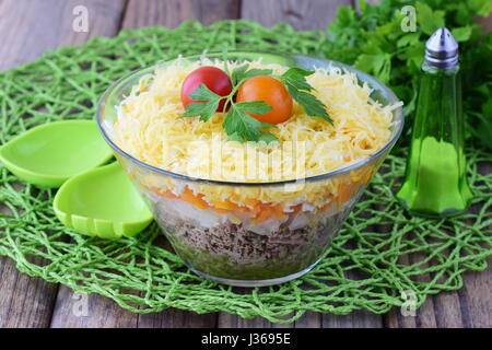 Salat mit Geflügelleber in Schichten mit Gurken, gekochten Karotten, Ei, Käse in eine Glasschüssel auf einem schwarzen Hintergrund abstrakt. Ansicht von oben. Gesunde Ernährung-Konzept. Stockfoto