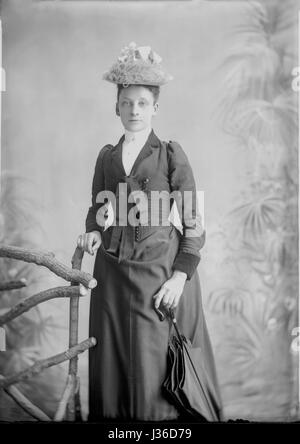 Studio Portrait eines viktorianischen Dame in einem langen dunklen Kleid und einen kleinen Hut auf einem Stuhl lehnte sich zurück. Im Jahr 1900 ergriffen. Stockfoto