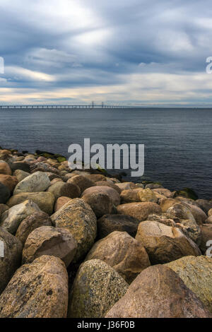 Große Felsen am Meeresufer, Seestück und Öresund-Brücke im Hintergrund an kalten Wintertag mit dramatischer Himmel Stockfoto