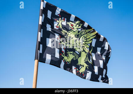 Schwarz / weiß karierte heraldische Flagge mit einem gelben Drachen in der mittleren flattern im Wind vor dem Hintergrund des blauen Himmels. Stockfoto