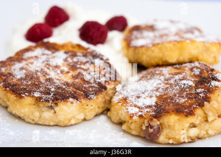 Syrniki (russische und ukrainische Pfannkuchen) serviert mit saurer Sahne und Himbeeren Stockfoto