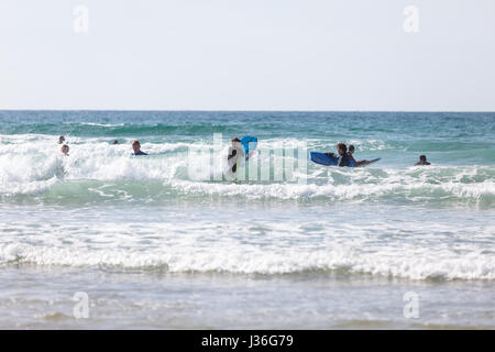 Newquay, Großbritannien. Strandurlauber geniessen Sie die Sonne auf einer hellen und sonnigen Frühling Nachmittag auf den Fistral Beach in Newquay. Die jungen Surfer body Boards Stockfoto