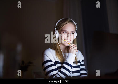 Frau mit Kopfhörern und Bleistift am Schreibtisch Stockfoto