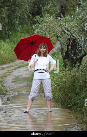 Roter Regenschirm, eine Frau im Regenpfützen auf dem Schlamm Weg Stockfoto