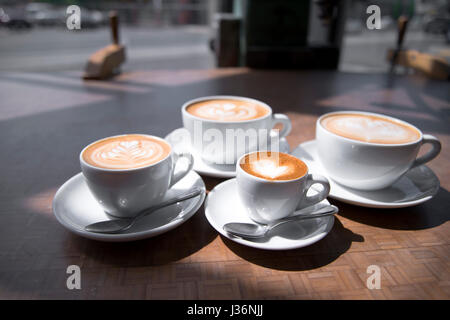 Kaffee Tassen mit Untertassen in verschiedenen Größen mit Karamell Bilder auf Schaum herzförmig und Blatt geformt für die ganze Familie Stockfoto