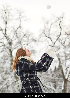 Schöne junge Mädchen tragen einen Wintermantel und werfen Schneeball in der Luft, Finnisch Wintertag im Februar Stockfoto