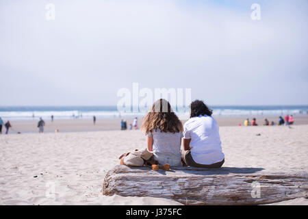 Zwei junge Menschen, Mann und Frau mit schönen lockiges Haar in Liebe auf alten an der Pazifikküste log sitzen und bewundern Sie die atemberaubende Landschaft Stockfoto