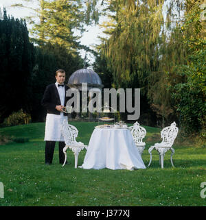 Kellner neben Esstisch im freien eingerichtet auf Rasen. Stockfoto