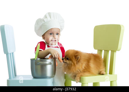 Role-playing Game. Kind Junge spielt Koch mit Hund. Kind weared Koch ernährt Spitz Welpen. Stockfoto