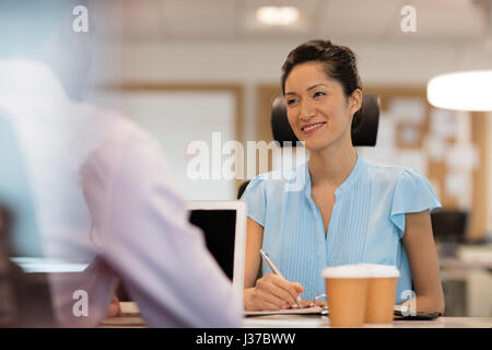 Lächelnde Geschäftsfrau diskutieren mit Kollegen im Büro durch Glas gesehen Stockfoto