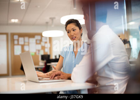 Geschäftsfrau, die Diskussion mit Kollegen während der Arbeit im Büro gesehen Smartphonen Glas Stockfoto