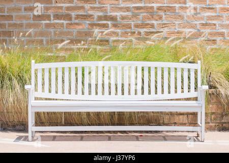 Weiße lange Stuhl vor dem Hintergrund der Gras- und Ziegel Wand. Stockfoto