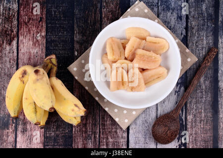 Thai beliebtes Dessert, fertig gekochte Banane in Sirup serviert und Löcher Banane serviert auf Holz. Stockfoto