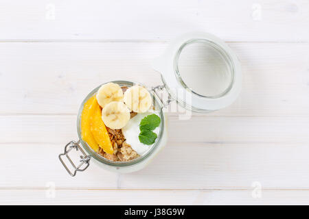 Glas mit Müsli mit Joghurt und frischem Obst auf weißem Hintergrund Stockfoto