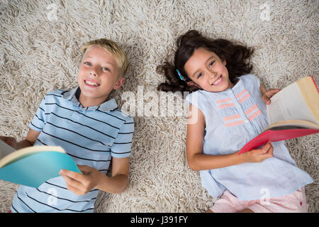 Geschwister auf Teppich liegen und lesen buchen im Wohnzimmer zu Hause Stockfoto