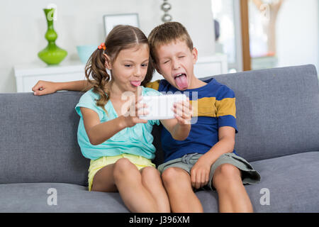 Geschwister unter Selfie auf Handy im Wohnzimmer zu Hause Stockfoto