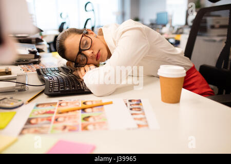 Müde Geschäftsfrau Nickerchen auf Schreibtisch im Kreativbüro Stockfoto