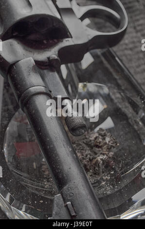 Pistole, Aschenbecher und Rauch. Rauchen kann tödlich sein. Gefahr. Stockfoto