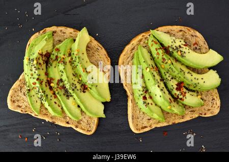 Offenen Avocado-Sandwiches mit Chia-Samen auf Vollkornbrot vor einem dunklen Hintergrund Schiefer Stockfoto